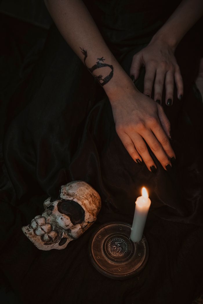 Eerily lit scene with candle, skull, and tattooed hands creating a mysterious vibe.