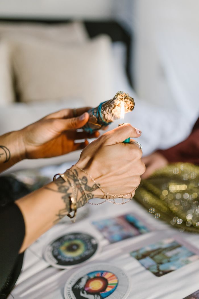 Close-up of tattooed hands lighting Palo Santo during a spiritual ritual indoors.